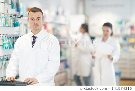Portrait of friendly male pharmacist at the cash register in pharmacy Portrait of friendly male pharmacist at the cash register in pharmacy 141974316