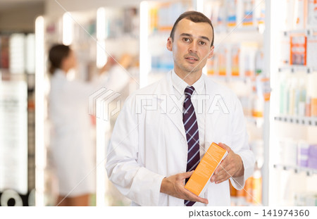 Young male pharmacist offering preparation in box Young male pharmacist offering preparation in box 141974360