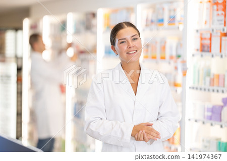 Young female pharmacist welcoming clients in chemist's shop Young female pharmacist welcoming clients in chemist's shop 141974367