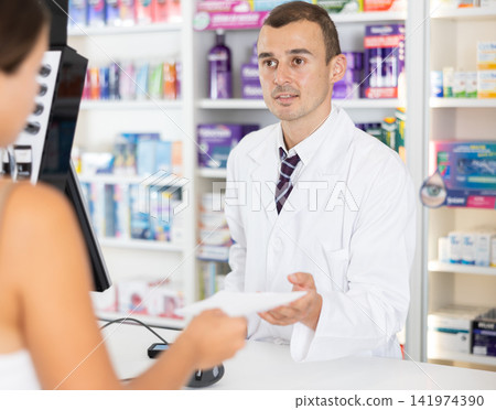 Young male pharmacist serving client buying medicament in drugstore Young male pharmacist serving client buying medicament in drugstore 141974390