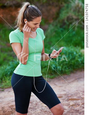 Outdoor, fitness and woman listening to music on mobile app for exercise, workout and training in forest. Person or runner with smartphone for audio streaming, podcast and health tracker in nature Outdoor, fitness and woman listening to music on mobile app for exercise, workout and training in forest. Person or runner with smartphone for audio streaming, podcast and health tracker in nature 141974758