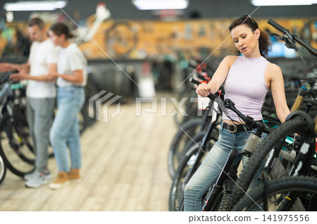 Active woman in bicycle shop chooses sports bike from range Active woman in bicycle shop chooses sports bike from range 141975556