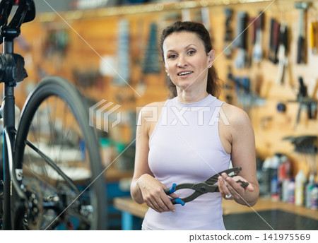 Smiling cyclist woman holding cassette pliers in bike workshop Smiling cyclist woman holding cassette pliers in bike workshop 141975569