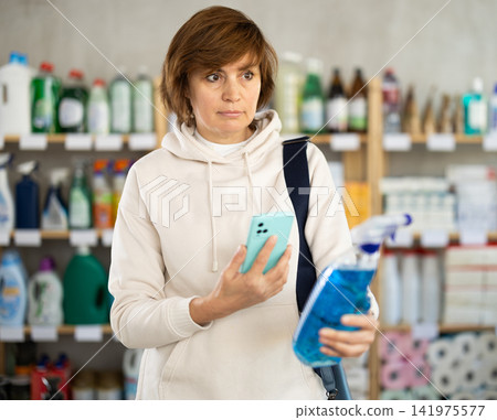 Checking expiration date of spray glass cleaner for windows - female shopper scans QR code on label of spray glass cleaner for windows using smartphone Checking expiration date of spray glass cleaner for windows - female shopper scans QR code on label of spray glass cleaner for windows using smartphone 141975577