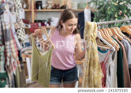 Positive teenage girl choosing something for summer in clothing store Positive teenage girl choosing something for summer in clothing store 141975595