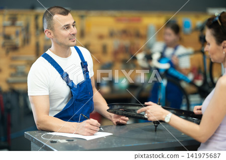 Young experienced man seller taking order and talking with woman client about bicycle in workshop 141975687