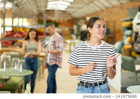 Girl look for something in furniture store, searching for perfect item to complete patio Girl look for something in furniture store, searching for perfect item to complete patio 141975690