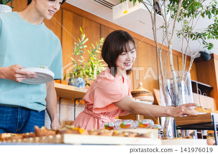 A young couple choosing dishes at a buffet-style lunch. A young couple choosing dishes at a buffet-style lunch. 141976019