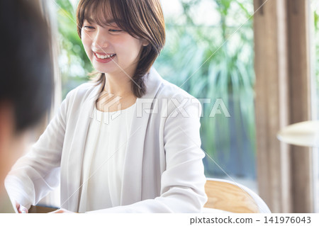 A female business person listening attentively with a smile in a brightly lit office. A female business person listening attentively with a smile in a brightly lit office. 141976043