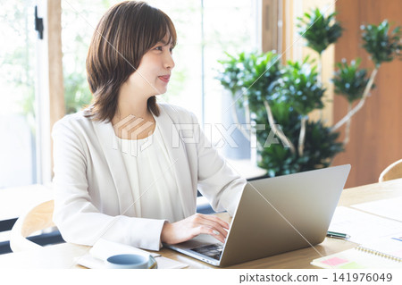 A smiling businesswoman in a brightly lit office, working on her laptop. A smiling businesswoman in a brightly lit office, working on her laptop. 141976049