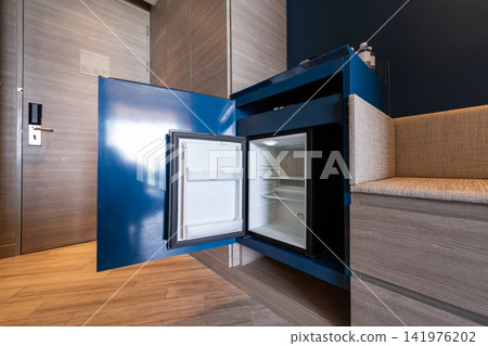 Hotel black minibar refrigerator guest room features a mini fridge neatly placed beneath a blue wooden desk, functional workspace with convenient in contemporary room. Hotel black minibar refrigerator guest room features a mini fridge neatly placed beneath a blue wooden desk, functional workspace with convenient in contemporary room. 141976202