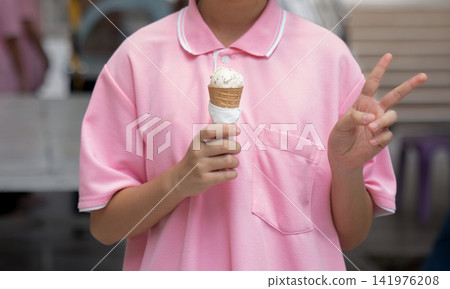 A young person holds a waffle ice cream cone and shows a victory hand gesture. A young person holds a waffle ice cream cone and shows a victory hand gesture. 141976208