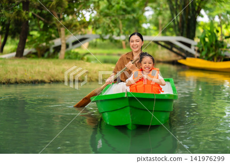 mother and preschool child girl in a green paddle boat on a scenic pond. mother and preschool child girl in a green paddle boat on a scenic pond. 141976299