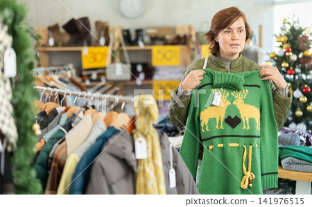 Woman chooses fashionable sweater for winter season in shop Woman chooses fashionable sweater for winter season in shop 141976515