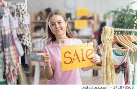 Teenage girl holding sale banner in clothing store 141976568