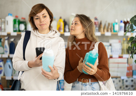 Two women checking expiration date of shampoo or shower gel using her smartphone in supermarket Two women checking expiration date of shampoo or shower gel using her smartphone in supermarket 141976610