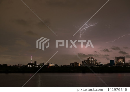 Discharge within clouds during a sudden thunderstorm; the city's night view illuminated by lightning. Discharge within clouds during a sudden thunderstorm; the city's night view illuminated by lightning. 141976846