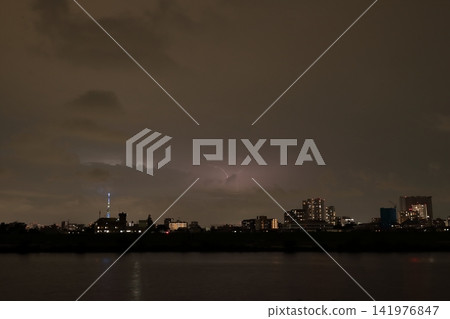 Discharge within clouds during a sudden thunderstorm; the city's night view illuminated by lightning. Discharge within clouds during a sudden thunderstorm; the city's night view illuminated by lightning. 141976847