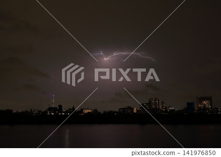 Discharge within clouds during a sudden thunderstorm; the city's night view illuminated by lightning. Discharge within clouds during a sudden thunderstorm; the city's night view illuminated by lightning. 141976850