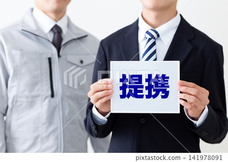 一位身著西裝的年輕商人,和一位身穿工作服、手持白板的中年男子,共同代表合作關係。 一位身著西裝的年輕商人,和一位身穿工作服、手持白板的中年男子,共同代表合作關係。 141978091
