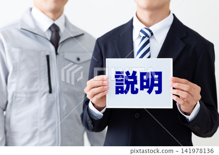 一位身穿西裝的年輕商人,手持一塊寫著說明的白板;還有一位身穿工作服的中年男子。 一位身穿西裝的年輕商人,手持一塊寫著說明的白板;還有一位身穿工作服的中年男子。 141978136
