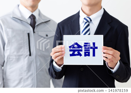 一位身穿西裝、手持會計白板的年輕商人,以及一位身穿工作服的中年男子。 一位身穿西裝、手持會計白板的年輕商人,以及一位身穿工作服的中年男子。 141978159