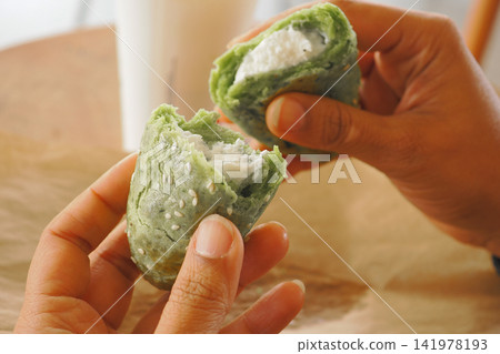 a person breaking open a soft, chewy green-tinted mochi pastry  141978193