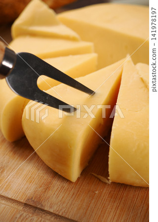 Cheese is being sliced on a wooden board with a fork 141978197