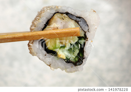 Sushi roll held with chopsticks in a dining setting Sushi roll held with chopsticks in a dining setting 141978228