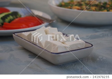 Soft cheese served at a meal with vegetables on the table 141978235