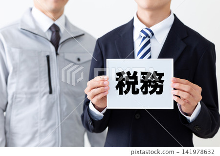 A young businessman in a suit holding a tax whiteboard and a middle-aged man in work clothes. A young businessman in a suit holding a tax whiteboard and a middle-aged man in work clothes. 141978632