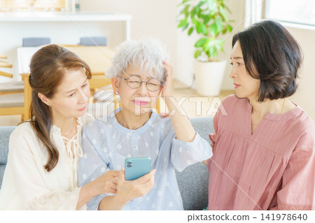A Japanese senior woman is holding her smartphone and clutching her head, while another woman watches over her. A Japanese senior woman is holding her smartphone and clutching her head, while another woman watches over her. 141978640