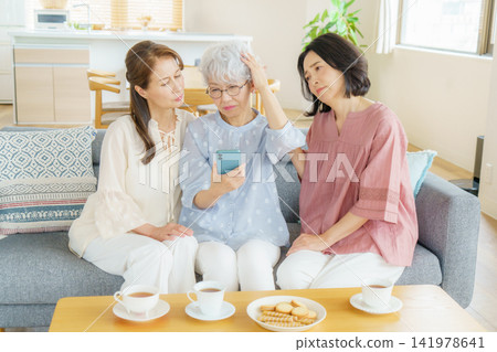 A Japanese senior woman is holding her smartphone and clutching her head, while another woman watches over her. A Japanese senior woman is holding her smartphone and clutching her head, while another woman watches over her. 141978641