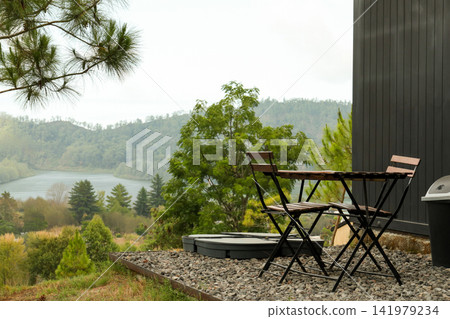 Cozy table and chairs set up beside the river surrounded by trees Cozy table and chairs set up beside the river surrounded by trees 141979234