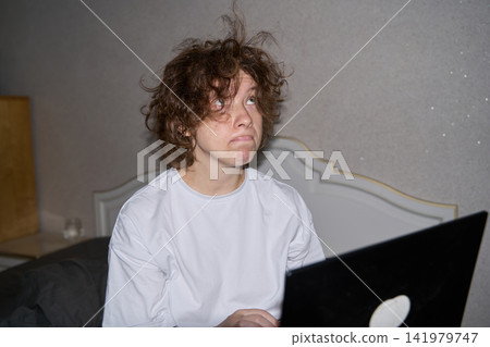 Woman Looking Away From Laptop With Tired Expression While Sitting In Bedroom Workspace Woman Looking Away From Laptop With Tired Expression While Sitting In Bedroom Workspace 141979747