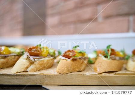 Sliced Baguette Pieces Topped With Cherry Tomatoes Basil And Creamy Spread Placed On Wooden Cutting Sliced Baguette Pieces Topped With Cherry Tomatoes Basil And Creamy Spread Placed On Wooden Cutting 141979777