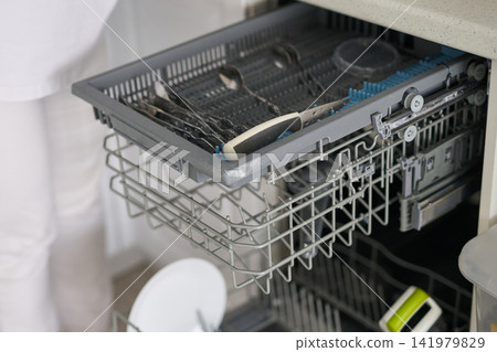 Person Loading Utensils Into Upper Cutlery Tray Of Open Dishwasher In Modern White Kitchen Near Person Loading Utensils Into Upper Cutlery Tray Of Open Dishwasher In Modern White Kitchen Near 141979829