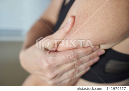 Middle-Aged Woman Holding Upper Arm In Discomfort During Indoor Closeup Self Examination In Sports Middle-Aged Woman Holding Upper Arm In Discomfort During Indoor Closeup Self Examination In Sports 141979857