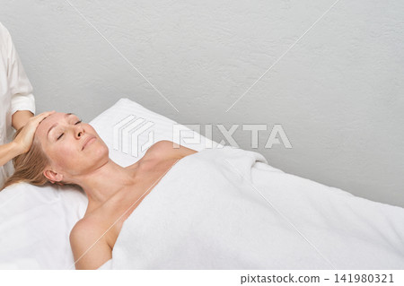 Woman Resting During Head Massage On Treatment Table In Bright Spa Room With White Bedding Woman Resting During Head Massage On Treatment Table In Bright Spa Room With White Bedding 141980321