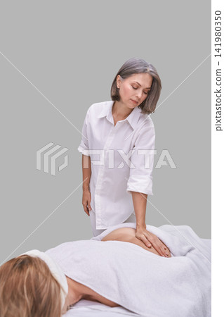 Female Therapist Pressing Lower Back Of Prone Client During Massage Session On Treatment Table Female Therapist Pressing Lower Back Of Prone Client During Massage Session On Treatment Table 141980350