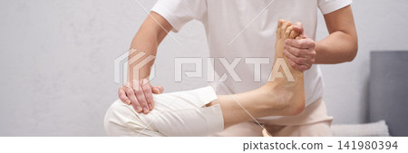 Therapist Holding Client Foot And Guiding Assisted Stretch While Client Lies On Mat With Neutral Therapist Holding Client Foot And Guiding Assisted Stretch While Client Lies On Mat With Neutral 141980394