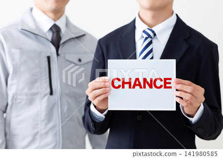 A young businessman in a suit holding a whiteboard that says CHANCE, and a middle-aged man in work clothes. A young businessman in a suit holding a whiteboard that says CHANCE, and a middle-aged man in work clothes. 141980585