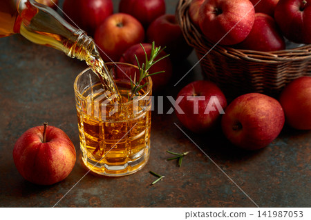 Apple juice is poured from a bottle into a glass. Apple juice is poured from a bottle into a glass. 141987053