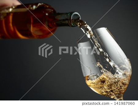 Pouring white wine from a bottle into a glass. Pouring white wine from a bottle into a glass. 141987060