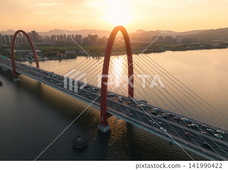 Traffic flows over red bridge as the golden sunset glows off the Qiantang River and the urban skyline. Traffic flows over red bridge as the golden sunset glows off the Qiantang River and the urban skyline. 141990422