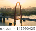 Golden sunset over Hangzhou Qiantang River bridge, with traffic crossing and city skylines reflecting on the water 141990425
