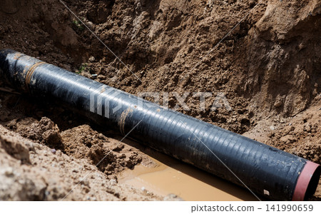 large black industrial pipe in dirt trench. large black industrial pipe in dirt trench. 141990659
