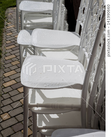Stacked wet white chiavari chairs with water drops outdoors. Stacked wet white chiavari chairs with water drops outdoors. 141990660