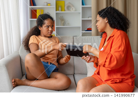 Mother and daughter pulling tablet between them in playful tug of war 141990677