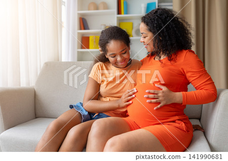 Smiling black pregnant mother and daughter bonding together, girl touching moms belly 141990681